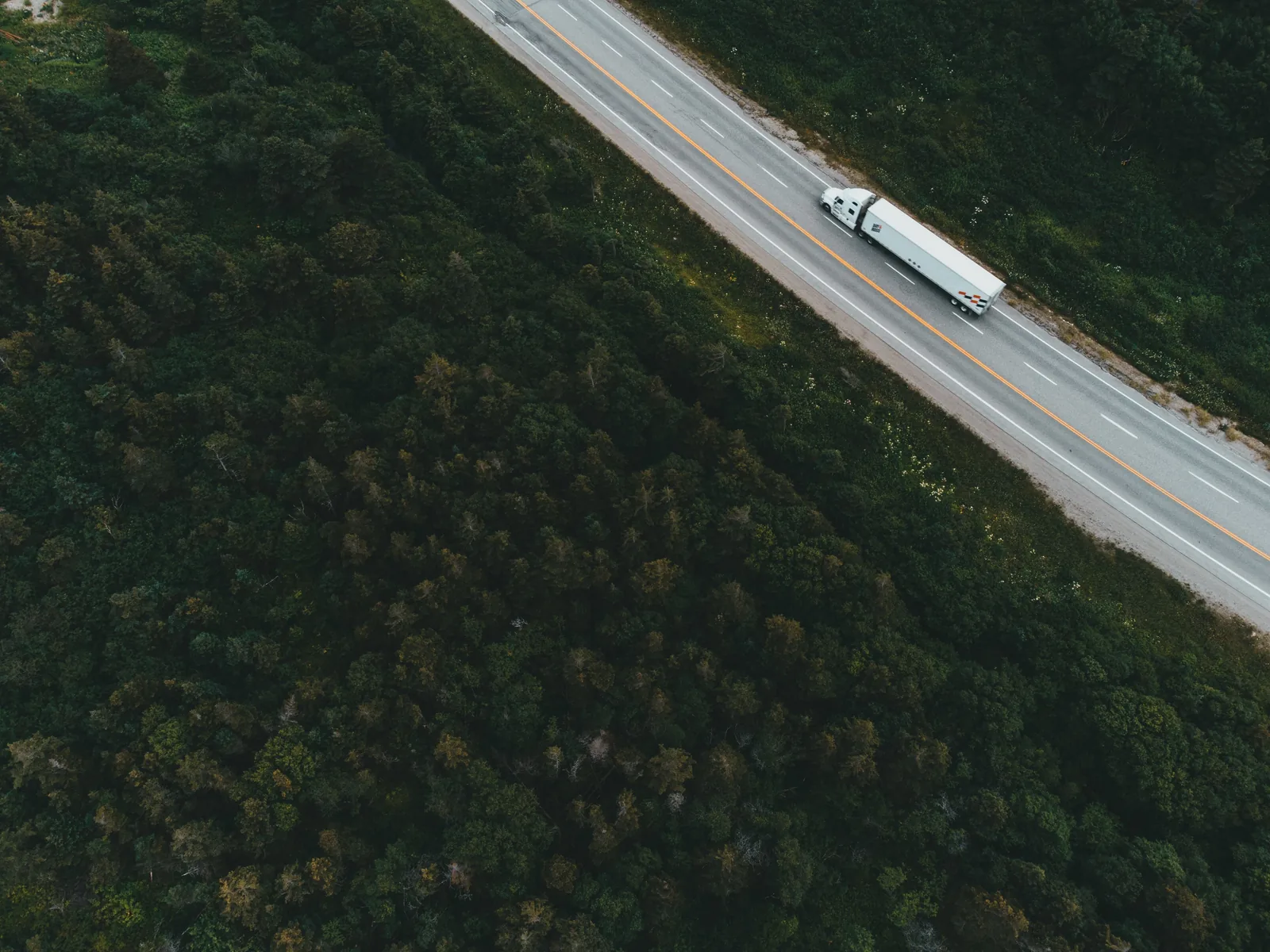 Aerial photograph of a white freight truck on a tree-lined road